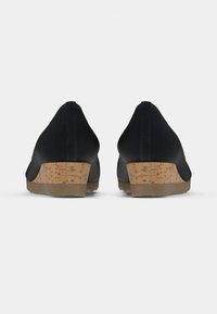 Paire de talons compensés noirs avec semelles de hauteur moyenne à texture liège, vus de dos sur un fond clair uni.