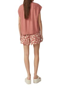 Kurze, rosa Leinenbluse, kombiniert mit gemusterten, korallenfarbenen Shorts mit einem abstrakten Creme-Muster. Das Model trägt beigefarbene Plateausandalen.