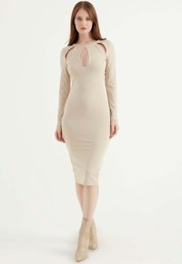 Beiges langärmeliges Kleid mit einem Schlüsselloch-Ausschnitt und figurbetonter Silhouette. Hergestellt aus glattem Stoff, reicht es bis zur Mitte der Waden und wird mit beigen Knöchelstiefeln kombiniert.