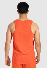 Pomarańczowy top na ramiączkach wykonany z bawełny, z okrągłym dekoltem i szerokimi wycięciami na ramionach, pokazany z tyłu, o gładkiej, jednolitej fakturze.