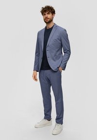 Blazer azzurro chiaro e pantaloni coordinati in tessuto textured, abbinati a una t-shirt scura e completati da sneakers bianche.