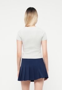 Világosszürke, rövidujjú ing, tengerészkék, pliszírozott szoknyával párosítva. Simma anyag, testhezálló kialakítással, ami egy laza és modern megjelenést sugall.