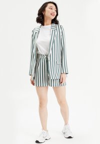 Ensemble blazer et short rayé avec des rayures verticales vertes et blanches, en tissu léger, doté d'un col classique et de poches. T-shirt blanc en dessous.