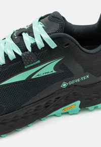 Fekete és türkiz futócipő, texturált hálós felsőrésszel, GORE-TEX címkével, Vibram talppal és kontrasztos fűzőkkel. Funkciógazdag kialakítás a tartósság érdekében.