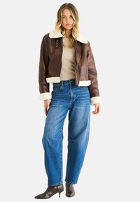 Brown leather bomber jacket with white shearling collar and cuffs, paired with high-waisted blue jeans and snake print heeled boots.