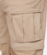 Beige cargobyxor med en stor veckad ficka, sydda detaljer och en slät yta. Fodrad ficka med dragkedja ovanför viken.