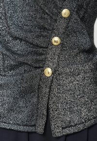 Metaliczna czarna dzianinowa bluzka o fakturowanym wykończeniu. Złote guziki, marszczone detale oraz dół sięgający powyżej talii.