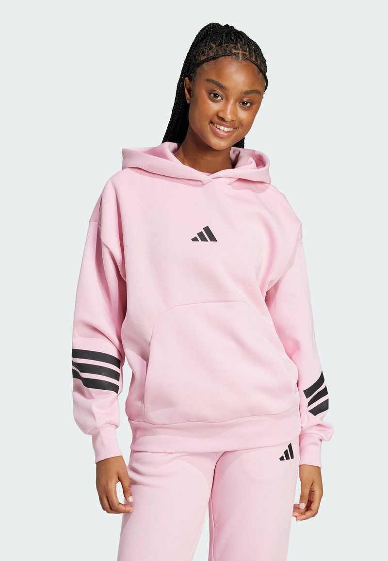 Ροζ φούτερ με κουκούλα, με μαύρο λογότυπο Adidas και τρεις ρίγες στα μανίκια. Φτιαγμένο από μαλακό, υφασμάτινο υλικό. Διαθέτει μπροστινή τσέπη.