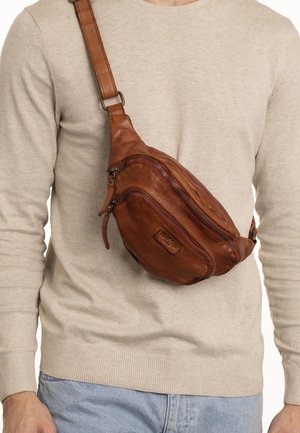Borsa a tracolla in pelle marrone con più scomparti con zip, tracolla regolabile e una texture liscia, indossata sul corpo sopra un maglione beige.