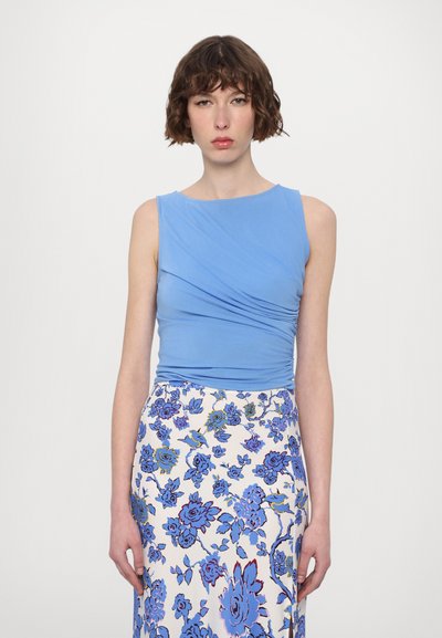 Haut sans manches bleu clair avec des détails froncés, associé à une longue jupe florale bleue et blanche, ornée de roses bleues et de vignes.