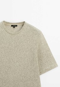 Vaaleanbeige lyhythihainen neulepaita pyöreällä pääntiellä, jossa on teksturoitu kangas ja hienovaraisia värivaihteluita ympäriinsä.