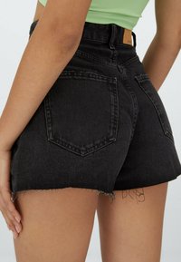 Mustat korkeavyötäröiset farkkushortsit, joissa on rispaantuneet reunat, kaksi takataskua ja vaalea nahkainen vyötärönauhamaissa oleva merkki.