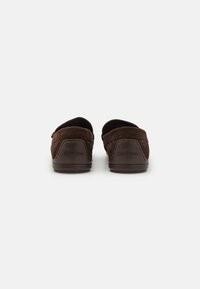 Brown suede slip-on shoes with rounded backs and rubber soles. Features minimal stitching and a subtle logo on the heel.