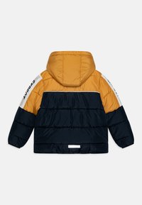 Veste rembourrée présentant un schéma de couleurs jaune et marine, avec une capuche, des poignets élastiques et une bande blanche avec du texte le long des manches.