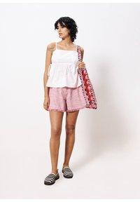 Witte mouwloze top met bloemenborduursel, gecombineerd met rood-witte gestreepte shorts met franjes aan de zoom. Vrouw met een gestreepte tote bag.