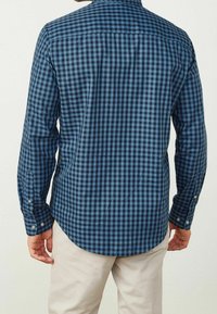 Niebieska koszula w kratę o różnych odcieniach niebieskiego, z długimi rękawami, mankietami zapinanymi na guziki oraz zaokrąglonym dołem. Wykonana z tkaniny o gładkiej fakturze.