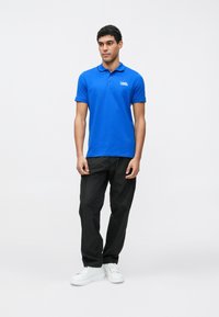 Svetlo modra polo majica s kratkimi rokavi in ovratnikom z logotipom, kombinirana s črnimi širokimi hlačami in belimi supergami.