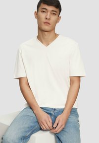 Weiße Baumwoll-T-Shirts mit V-Ausschnitt und kurzen Ärmeln, kombiniert mit hellblauen Jeans. Einfaches Design ohne sichtbare Muster oder Logos.