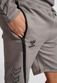Grå sportshorts med en zip-ficka, svarta detaljer och en Hummel-logotyp. Tyget har en texturerad yta och en bekväm passform.