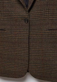 Blazer à carreaux marron et vert foncé avec une fermeture par un bouton noir et deux poches avant, montré de la poitrine à la taille.