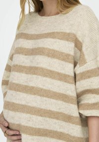 Svetr s volným střihem vyrobený z měkké tkaniny, s alternativně krémovými a béžovými vodorovnými pruhy. Kruhý výstřih a krátké rukávy.