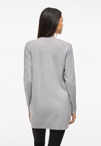 Grauer Strickcardigan mit langen Ärmeln aus weichem Strick, mit geripptem Saum und Bündchen, in lockerer Passform und einfarbig, getragen über schwarzen Leggings.