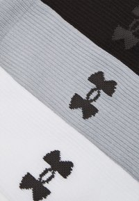 Tri páry športových ponožiek v čiernej, sivej a bielej farbe, s textúrovanou tkaninou a čiernym logom v tvare mašle na každom páre.