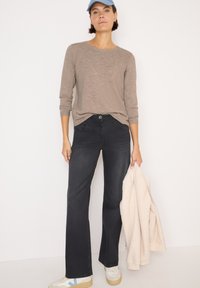 Jeans neri a zampa d'elefante, maglione beige a maniche lunghe a costine, giacca in pile crema e sneaker bianche con accenti blu. Design semplice, tessuti morbidi.