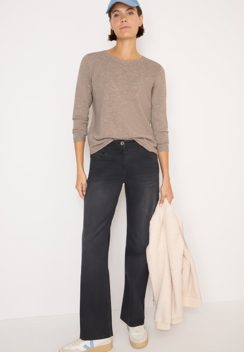 Jeans neri a zampa d'elefante, maglione beige a maniche lunghe a costine, giacca in pile crema e sneaker bianche con accenti blu. Design semplice, tessuti morbidi.