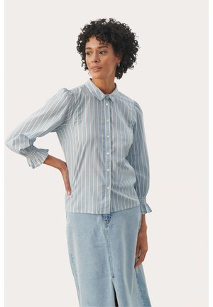 Chemise bleu clair rayée, à boutons, avec des manches bouffantes, un col arrondi et des poignets à volants, associée à une jupe en denim avec une fente devant.