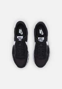Musta Nike-nike, joissa on verkko- ja synteettinen päällinen, valkoisia aksentteja, pyöreä kärki ja nauhakiinnitys. Pintakuvioitu ulkopohja pidon parantamiseksi.