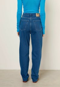 Hochtailler blauwe denim jeans met een relaxte pasvorm. Heeft twee achterzakken en een tan lederen label op de tailleband. Glad van structuur.