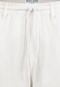 White linen shorts with an elastic waistband and white braided drawstring. Features two front pockets and a soft, textured fabric.