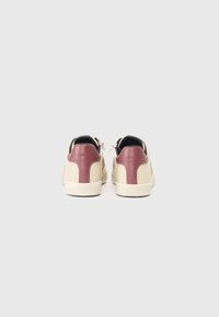 Sneaker con un corpo in pelle beige, dettagli in vernice bordeaux sul tallone e pannelli posteriori texturizzati. Presenta lacci piatti e una suola bianca a contrasto.