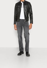 Chaqueta de cuero negra con cuello alto, cierre frontal con cremallera y dos bolsillos en el pecho, combinada con jeans grises y botines negros.