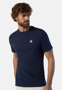 T-shirt in cotone blu navy con collo rotondo, maniche corte e un piccolo logo circolare sul lato sinistro del petto. Texture liscia e leggera.