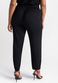 Zwarte, lichte broek met een elastische tailleband, tapered leg ontwerp en achterzakken, gecombineerd met strappy hoge hakken.