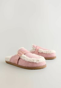 Lyserøde, fuzzy tøfler lavet af blødt filt med en hvid shearling kant, der har en lyserød rem og spænde samt en gummisål.