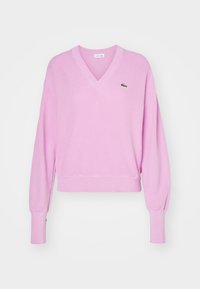 Suéter rosa de cuello en V, hecho de un tejido suave, con mangas largas y puños fruncidos, además de un pequeño logotipo verde en el lado izquierdo del pecho.