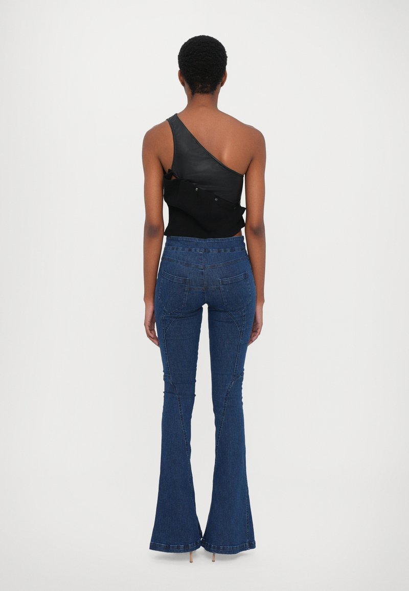 Schwarzes asymmetrisches Oberteil mit Lederdetails, kombiniert mit blauen Schlagjeans. Merkmale sind Nahtakzente und eine figurbetonte Taille.