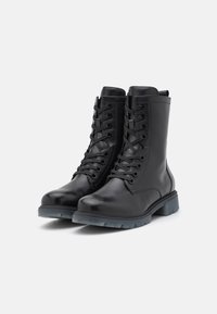 Botas de cuero negro hasta el tobillo con un acabado suave. Cuentan con puntera redonda, parte frontal con cordones y una suela de goma gruesa con un ligero dibujo.