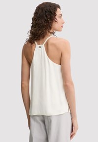 Top senza maniche color crema con una vestibilità rilassata, caratterizzato da un design con schiena bassa e un piccolo dettaglio metallico al colletto.
