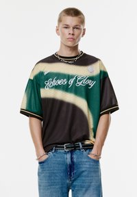 Korte mouwen shirt met een kleurverloop van groen, bruin en beige. Bevat "Echoes of Glory" in witte schrift en een hexagonaal textuurpatroon.