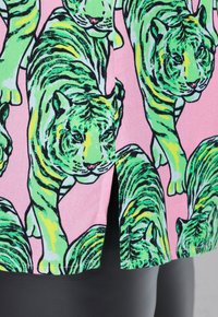 Rosa stof med et gentaget mønster af grønne og gule tigre. Glat tekstur med en let glans. Kanten har en slidsdetalje.