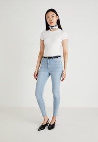 Απαλά μπλε skinny τζιν με ελαφριά φθορά, σε συνδυασμό με ένα εφαρμοστό λευκό T-shirt και μια μαύρη ζώνη. Συμπληρωμένα με μια διακοσμητική μαντήλα και μαύρα παπούτσια.