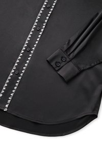 Camicia in satin nero con bottoni argentati, maniche lunghe con bottoni neri e orlo curvo. Texture liscia in tutto il capo.