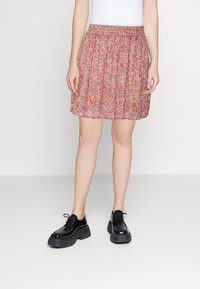 Falda con estampado floral y cinturilla elástica, que presenta tonos de rosa, rojo y azul. Diseño ligero y plisado; combinada con zapatos de plataforma negros.