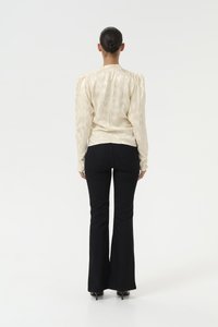 Light-colored, textured blouse with long sleeves and puff shoulders, paired with fitted black flared pants and heeled shoes.