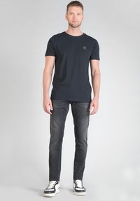 Camiseta negra con escote redondo, combinada con jeans oscuros y zapatillas en blanco y negro. Diseño simple, silueta ajustada y sin patrones visibles.