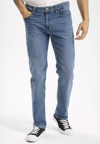 Jasnoniebieskie dżinsy o prostym kroju, pięć kieszeni, żółte szwy i klasyczne zapięcie na guzik, w połączeniu z czarnymi trampkami.